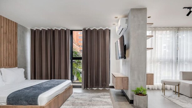 Un dormitorio moderno con una cama grande, un televisor montado en la pared y un balcón con cortinas.