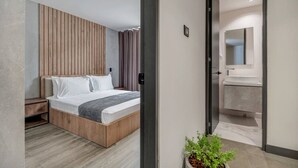 Quarto moderno com cabeceira de madeira, cama com roupa de cama branca, mesa de cabeceira e um vaso com planta.