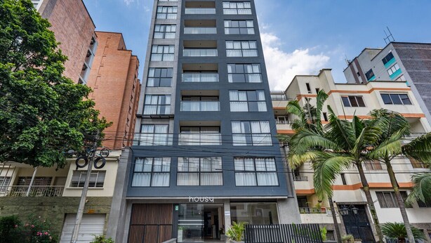 Um edifício moderno de vários andares, com entrada imponente, janelas amplas e uma placa visível com a inscrição "Housu".