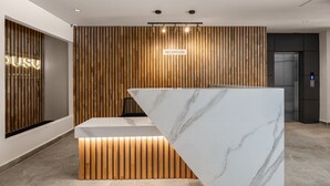 Uma receção moderna com bancada de mármore, ripas de madeira na parede e uma placa com a inscrição 'RECEPCIÓN'.