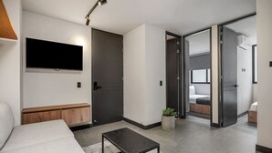 A modern hotel room with a flat-screen TV mounted on the wall, a wooden bench, a small table, and a potted plant. - Cozy 2BR apt in Laureles with AC and fast Wifi (Medellín)