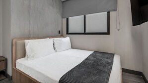 A modern hotel room with a large bed, a wooden headboard, a grey accent wall, and a flat-screen TV mounted on the wall. - Cozy 2BR apt in Laureles with AC and fast Wifi (Medellín)