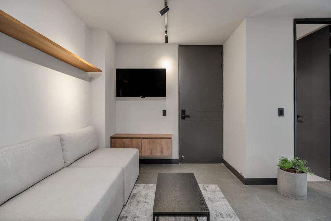 Een moderne woonkamer met een bank, een salontafel, een aan de muur bevestigde televisie en een deur.