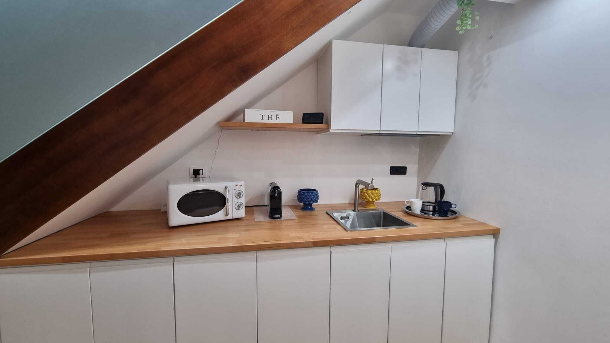 A compact kitchen with a microwave, kettle, and coffee maker on a wooden countertop.