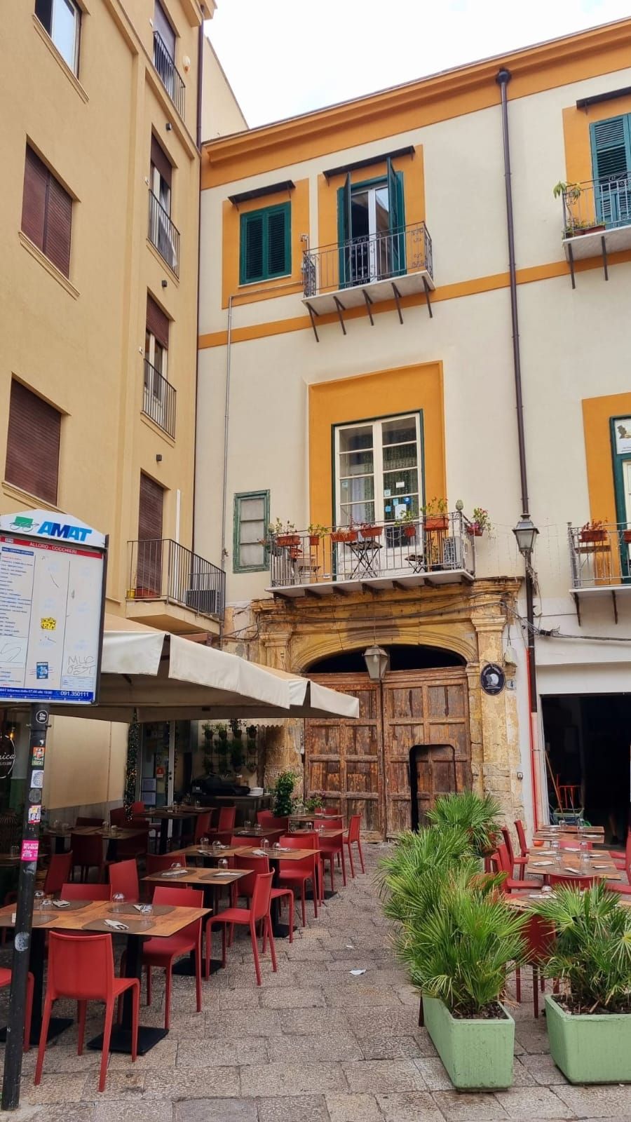 Ein Straßencafé mit Tischen und Stühlen, einer Holztür und einem Gebäude mit Balkonen und Fenstern.