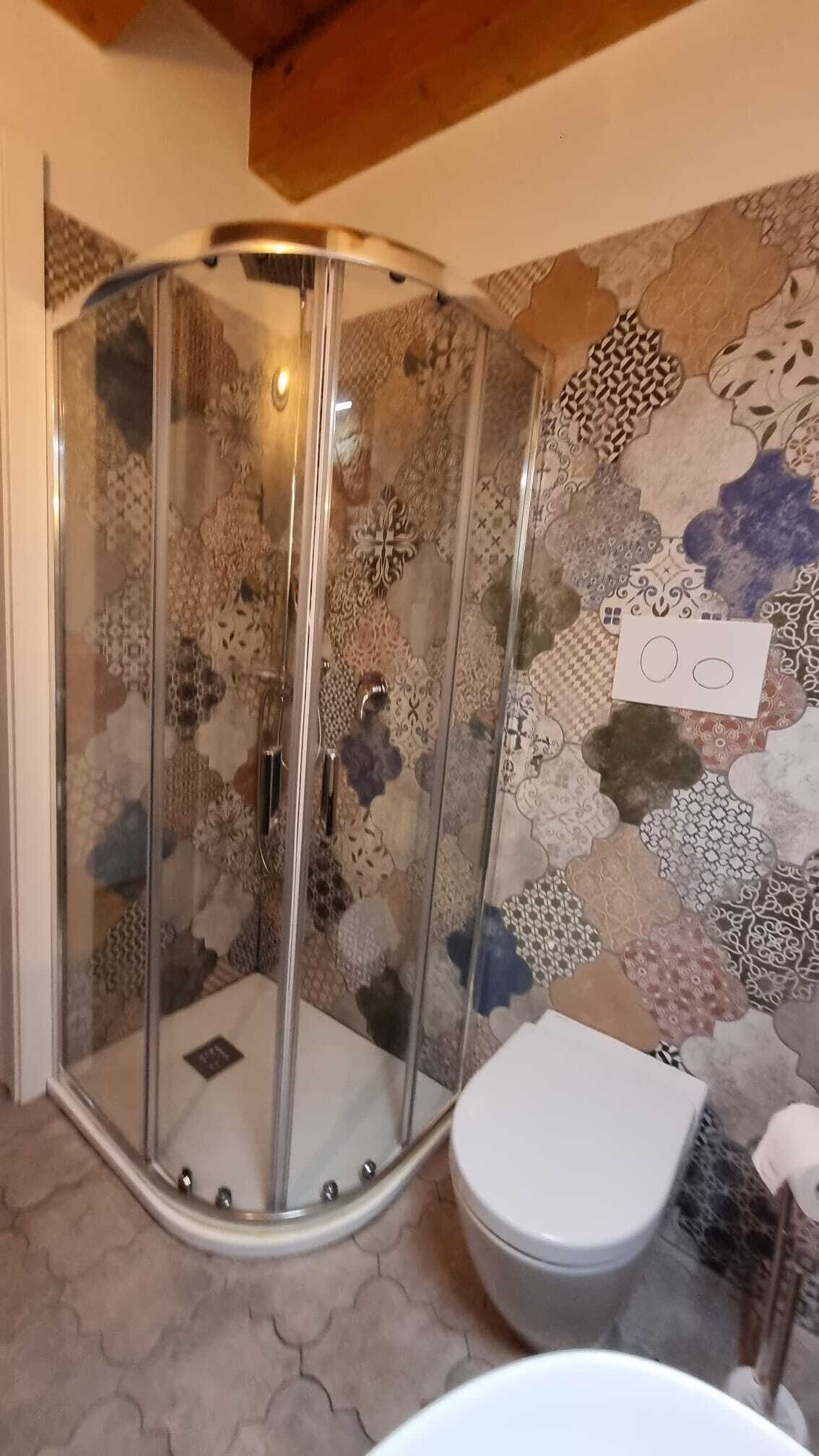A shower with a glass door, a toilet, and a patterned wall.