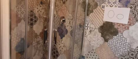 A shower with a glass door, a toilet, and a patterned wall.
