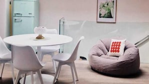 Un comedor moderno con una mesa redonda, sillas blancas, un sillón de peluche y un refrigerador azul claro.