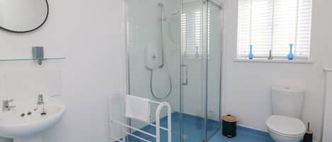 Een badkamer met een glazen douchecabine, een wit wastafelmeubel, een toilet en een raam met zonwering.