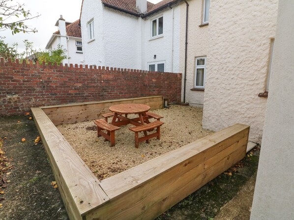 A wooden deck with a table and benches, surrounded by a gravel area and a brick wall.