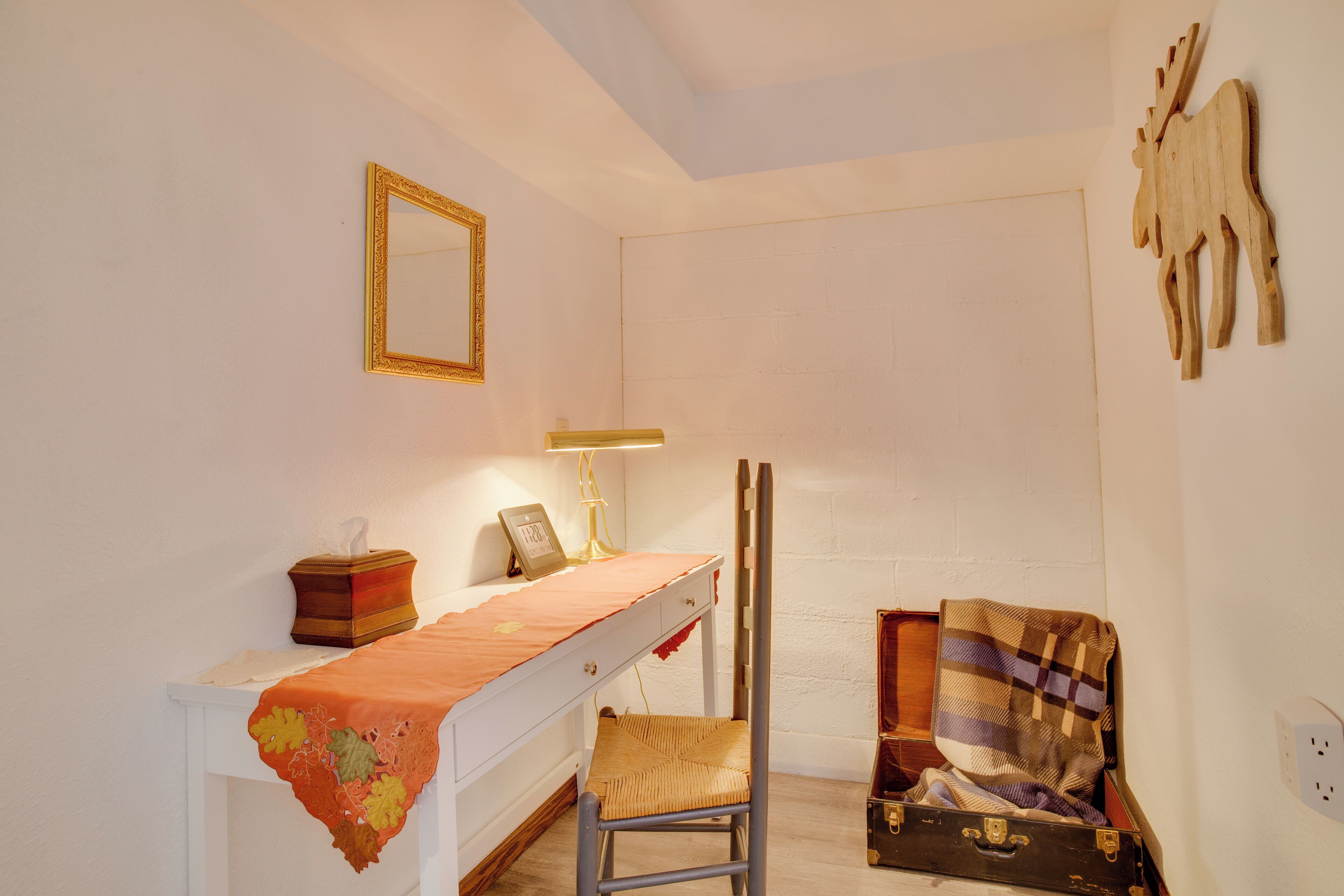 A room with a bed, a bedside table with a lamp, a mirror, and a wall-mounted wooden animal decoration.