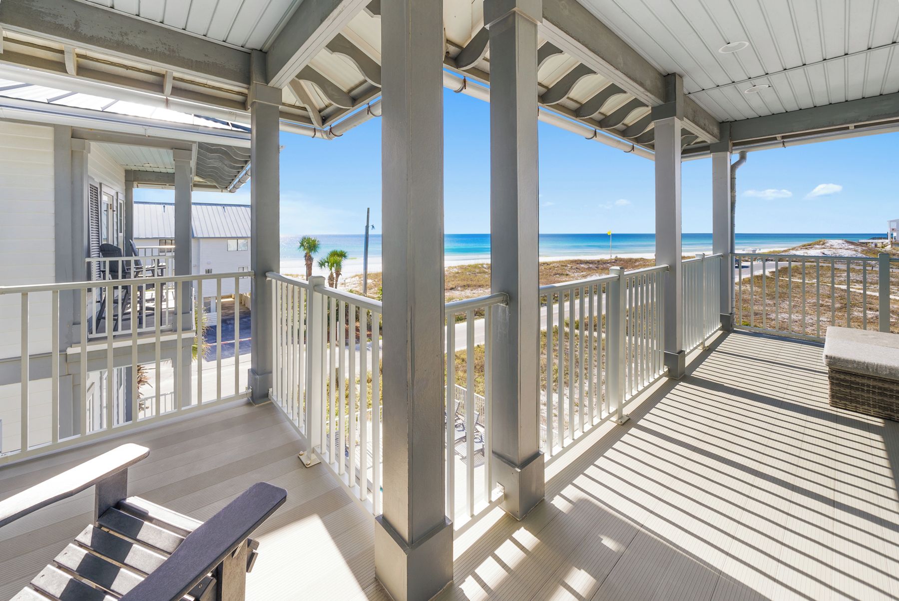 A covered outdoor area with a wooden deck, white railings, and a view of the beach.