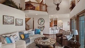 A spacious living area with a high ceiling, a staircase, and a dining area in the background.