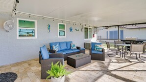 Une terrasse extérieure aménagée avec des meubles en osier, un barbecue et des guirlandes lumineuses.