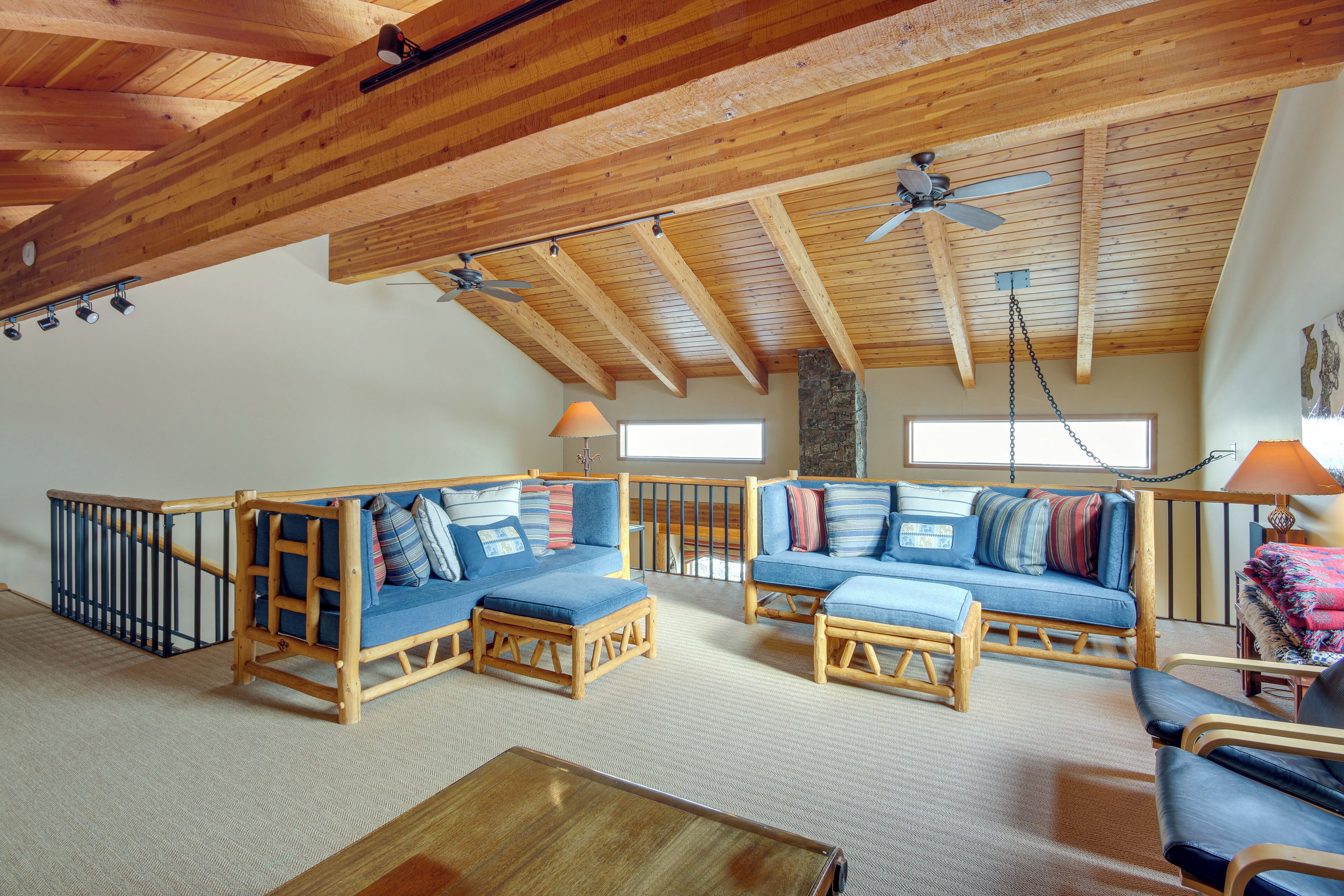 Un loft espacioso con techos altos y vigas de madera a la vista. Hay dos sofás azules con cojines, una mesa de centro de madera y una silla.