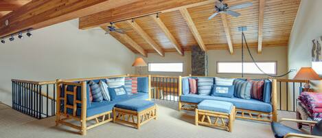 Un loft espacioso con techos altos y vigas de madera a la vista. Hay dos sofás azules con cojines, una mesa de centro de madera y una silla.