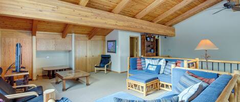 A cozy living room with a wooden ceiling, a sofa set, a dining table, and a TV.