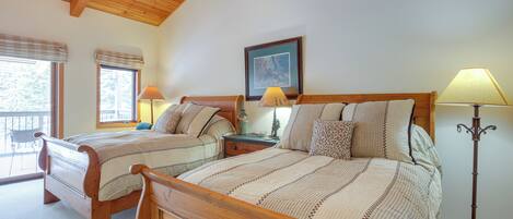Un dormitorio con dos camas de madera, una mesita de noche con lámparas, un cuadro enmarcado en la pared y una ventana con vistas.