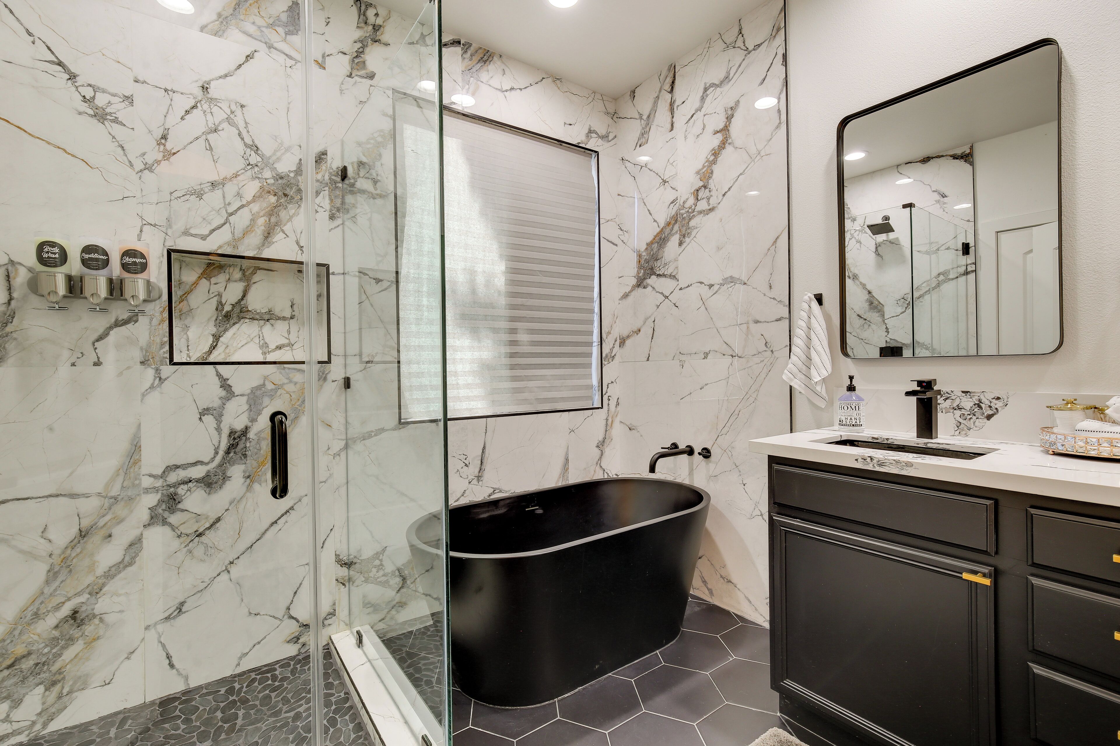 Ein modernes Badezimmer mit einer schwarzen, freistehenden Badewanne, einer Duschkabine aus Glas und einer Marmor-Spritzschutzwand.