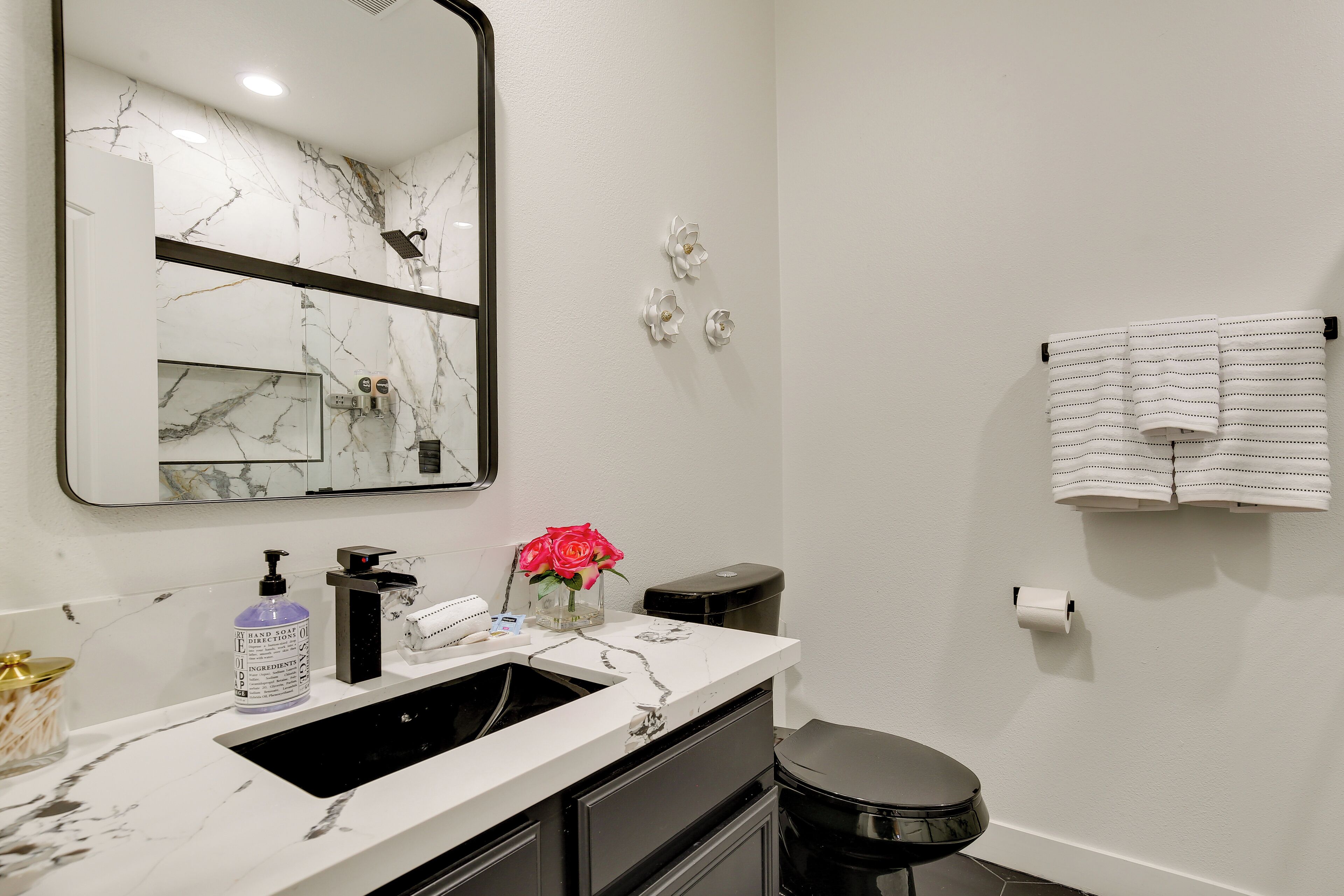 A bathroom with a white marble sink, a black toilet, a mirror with a marble backsplash, and a towel rack with a white towel.