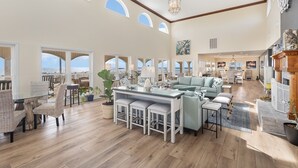 A spacious living area with a glass-top dining table, cushioned seating, and a view of the outdoors. - Alpha At The Point: Oceanfront, Private Pool & Hot Tub, Breathtaking Views (Garden City Beach)