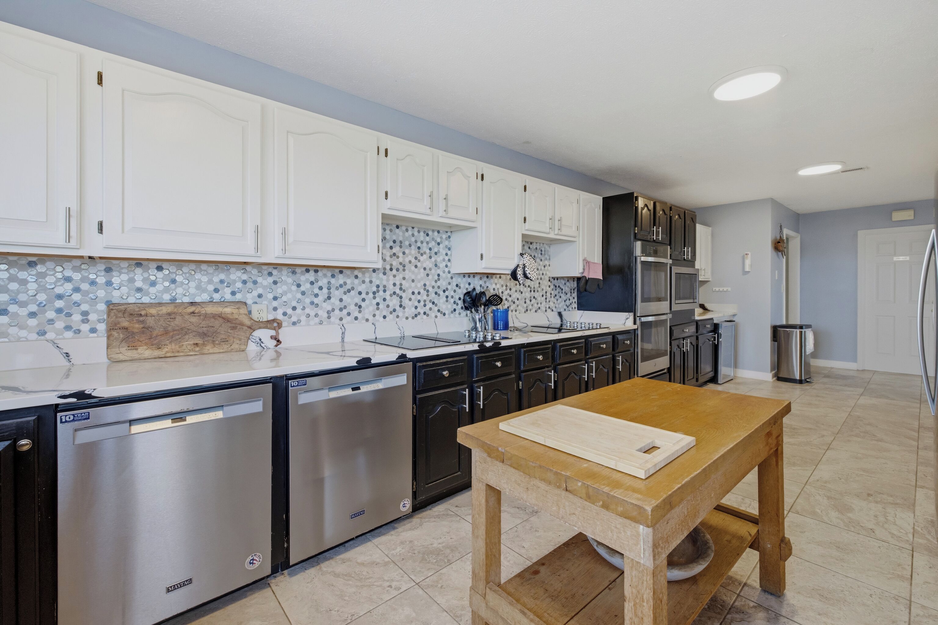 A modern kitchen with white cabinets, stainless steel appliances, and a wooden table.