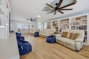 A spacious living room with a beige sofa, blue bean bags, and a bookshelf filled with books and decorative items.