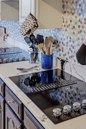 A kitchen with a glass backsplash, a blue utensil holder, and a stainless steel range hood.