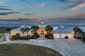 A beachfront house with a driveway, palm trees, and a view of the ocean.