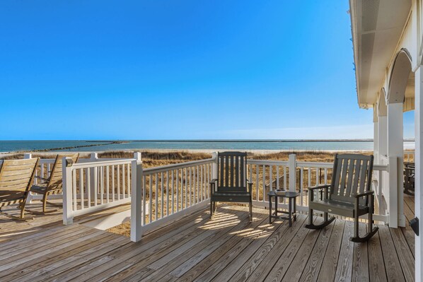 A wooden deck with chairs and a table overlooking a beach.