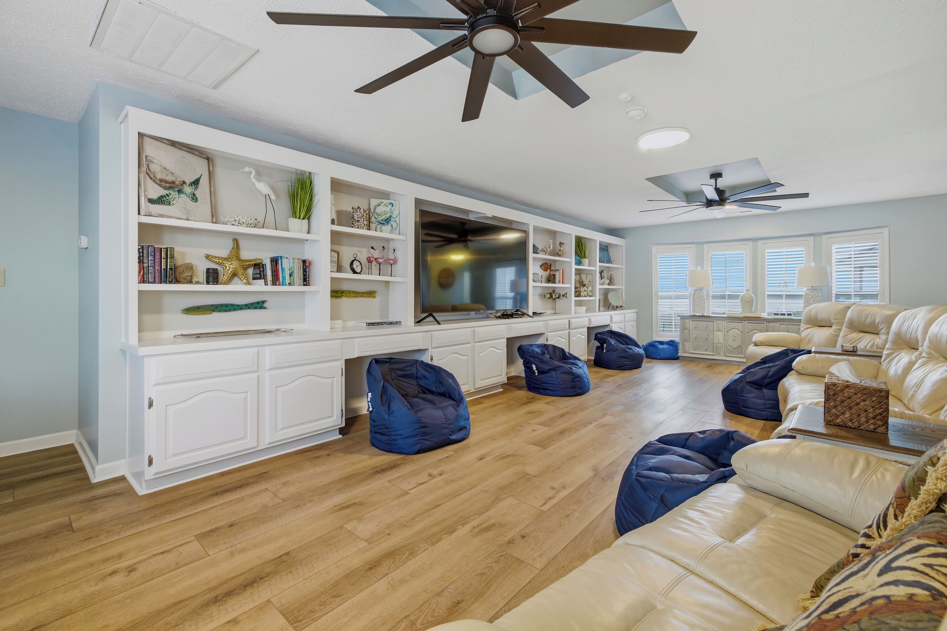 A spacious living room with a large TV, white built-in shelving, blue bean bags, and a beige sofa.