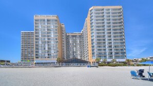 Un grand hôtel composé de plusieurs immeubles de grande hauteur, avec une plage au premier plan et un ciel bleu dégagé.