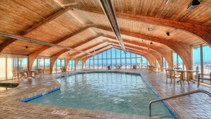 Une piscine intérieure avec un sol en briques et un plafond en bois, entourée de tables et de chaises.