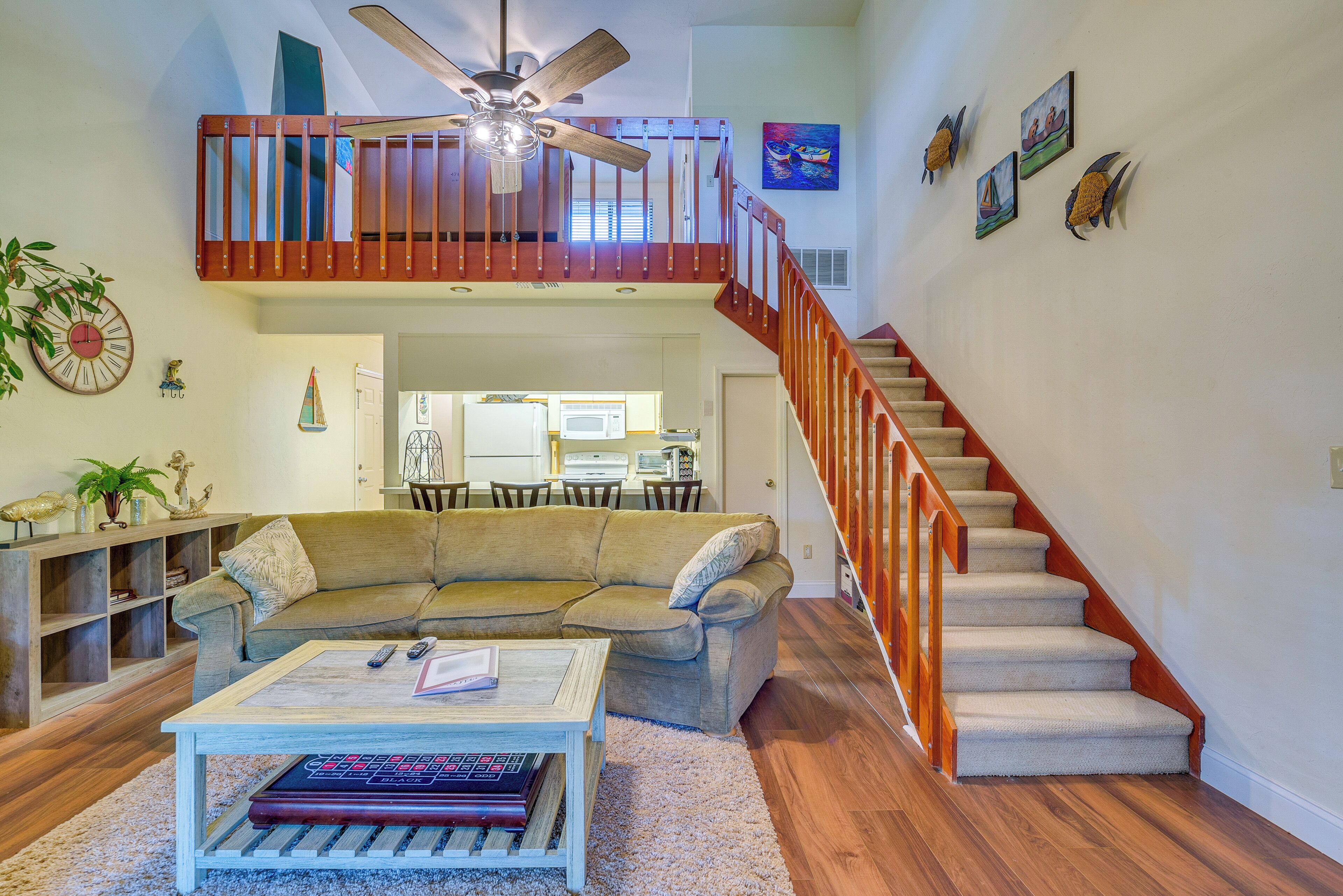 A spacious living room with a high ceiling, a wooden staircase, and a dining area in the background.