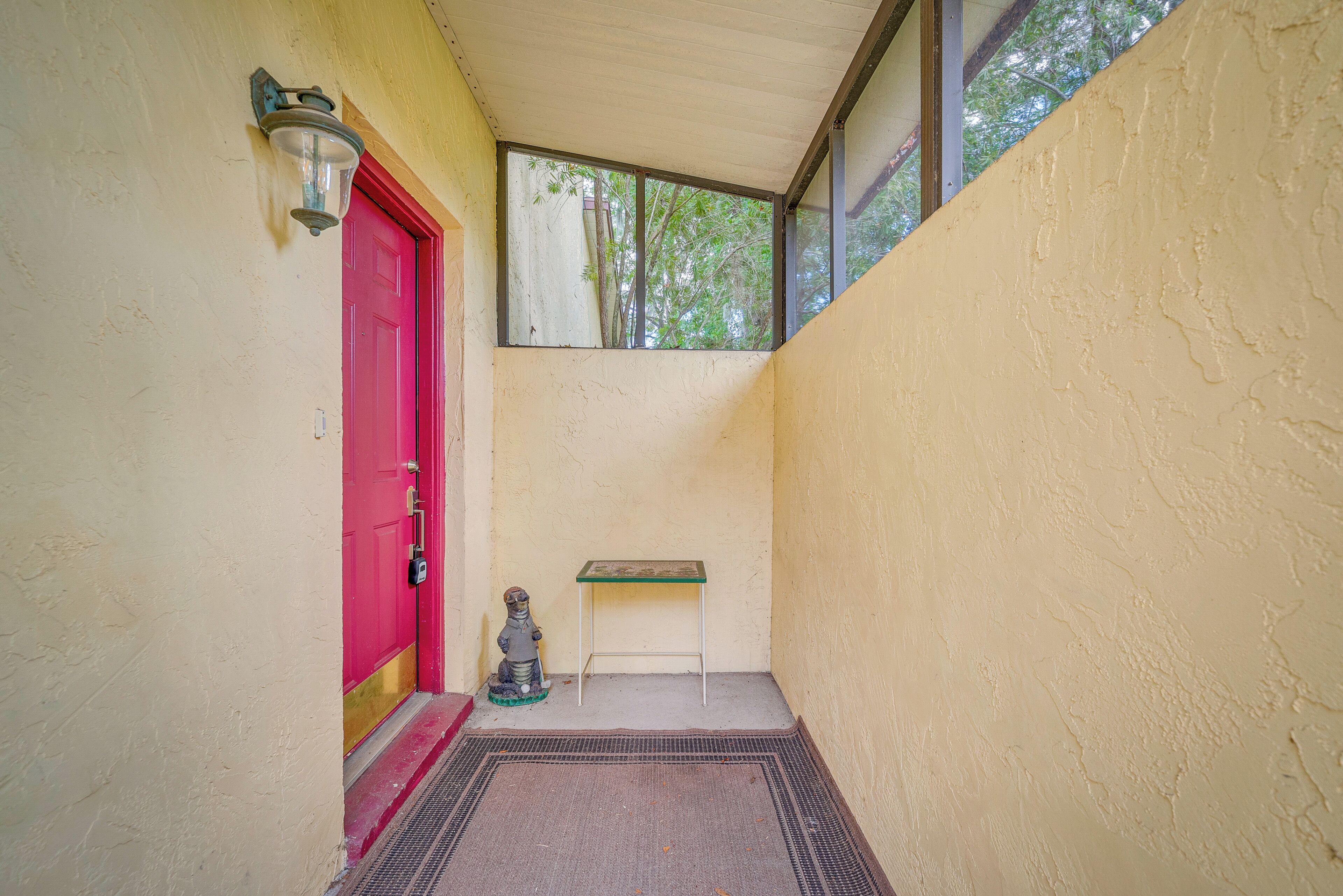 Un couloir étroit avec une porte rouge, une petite table et une statue.