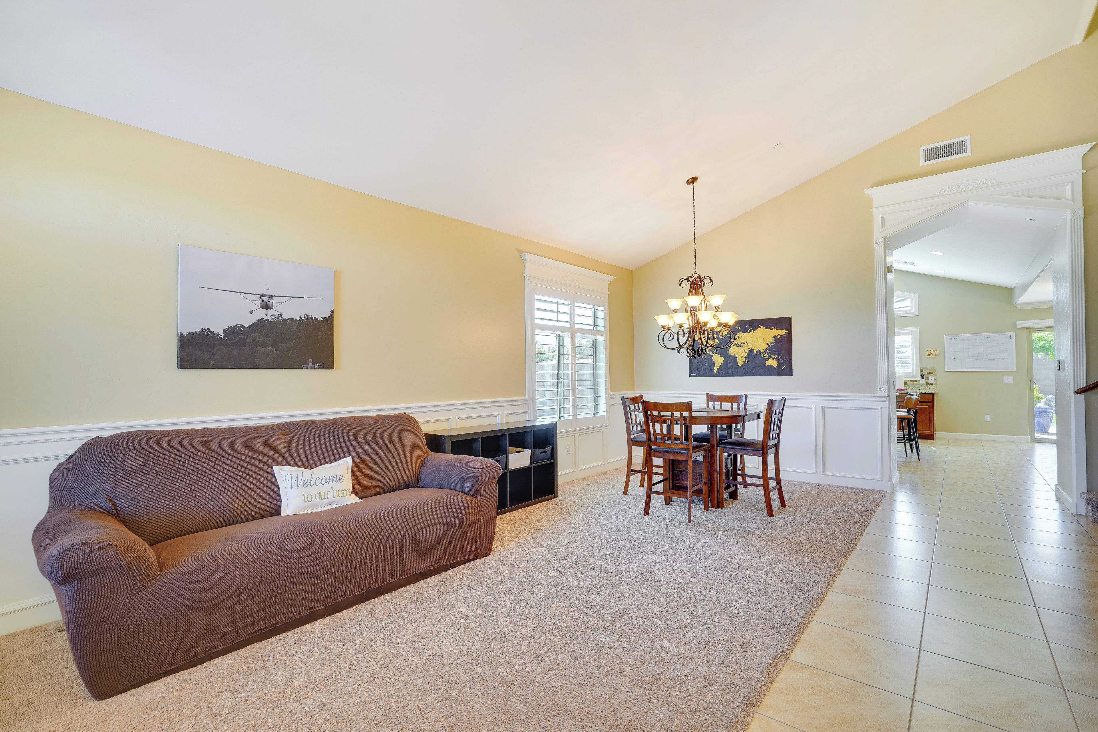 A living room with a brown sofa, a dining table with chairs, a chandelier, and a wall-mounted globe.