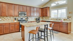 A kitchen with wooden cabinets, a central island with bar stools, a microwave, stove, and a large window with blinds. - Corona De Tucson Home With Hot Tub! (Vail)
