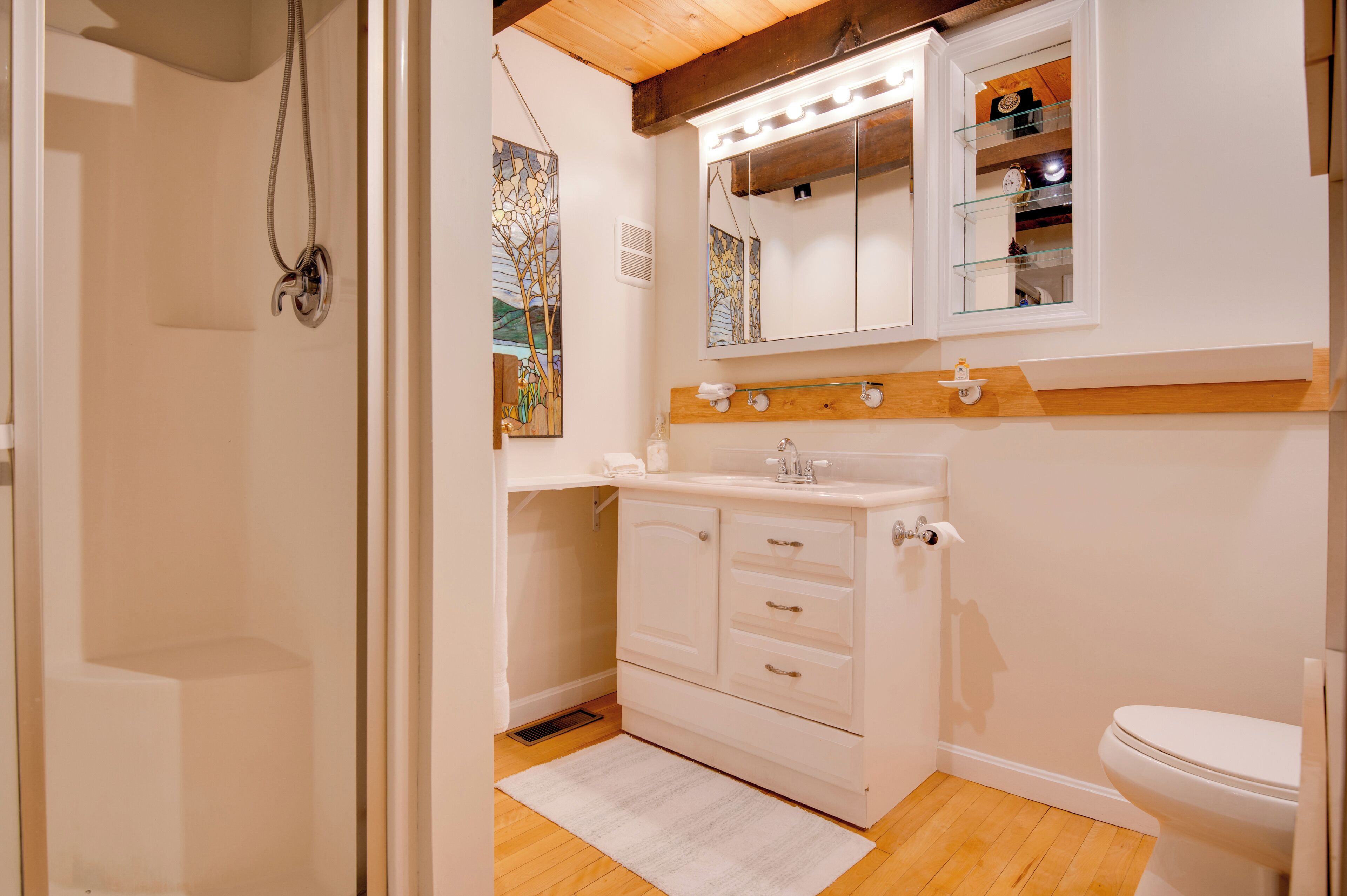 Une salle de bain avec une douche, un lavabo avec un miroir, des toilettes et une étagère en bois au-dessus du lavabo.