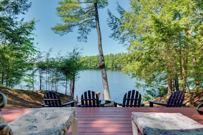 A deck with Adirondack chairs overlooking a lake, surrounded by trees. - Waterfront Lake Arrowhead Cabin w/ Dock & Fire Pit (North Waterboro)