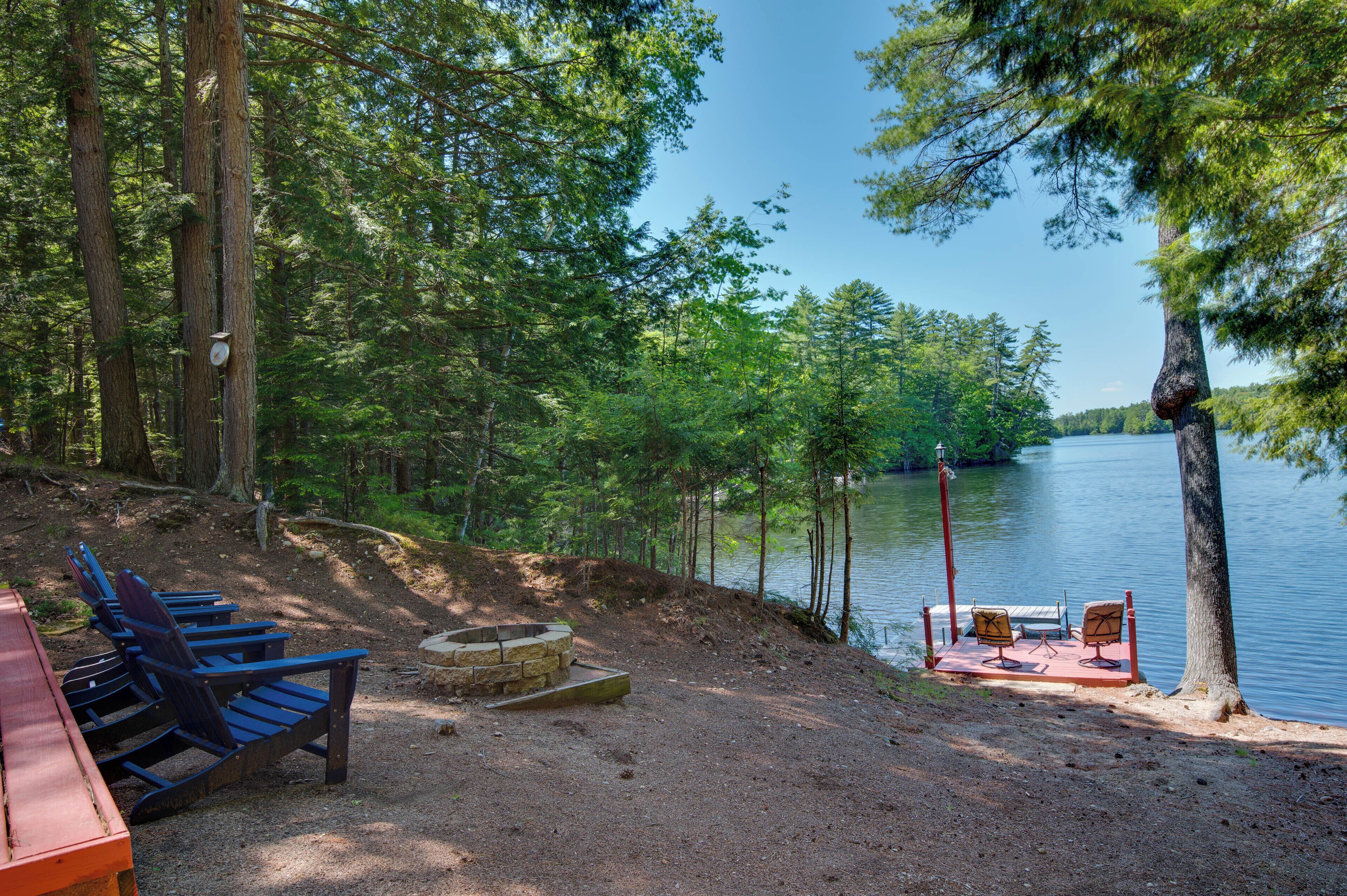 Un terrain de camping au bord du lac, équipé d’un foyer, de chaises et d’un banc situés près de l’eau.