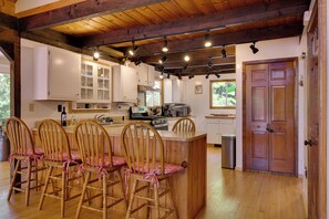 A kitchen with wooden chairs, a dining table, and a bar area. - Waterfront Lake Arrowhead Cabin w/ Dock & Fire Pit (North Waterboro)