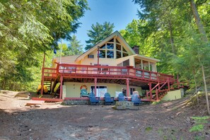 A lodge with a red balcony, multiple chairs, and a stone pathway leading to the entrance. - Waterfront Lake Arrowhead Cabin w/ Dock & Fire Pit (North Waterboro)
