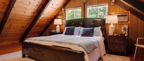 A bedroom with a wooden ceiling, a bed with a headboard, two bedside tables with lamps, and a window.