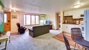 A living room with a sofa, a rocking chair, a dining table with chairs, and a kitchen area with cabinets and a refrigerator. - Lake Superior Getaway - Walk to Water! (Duluth)