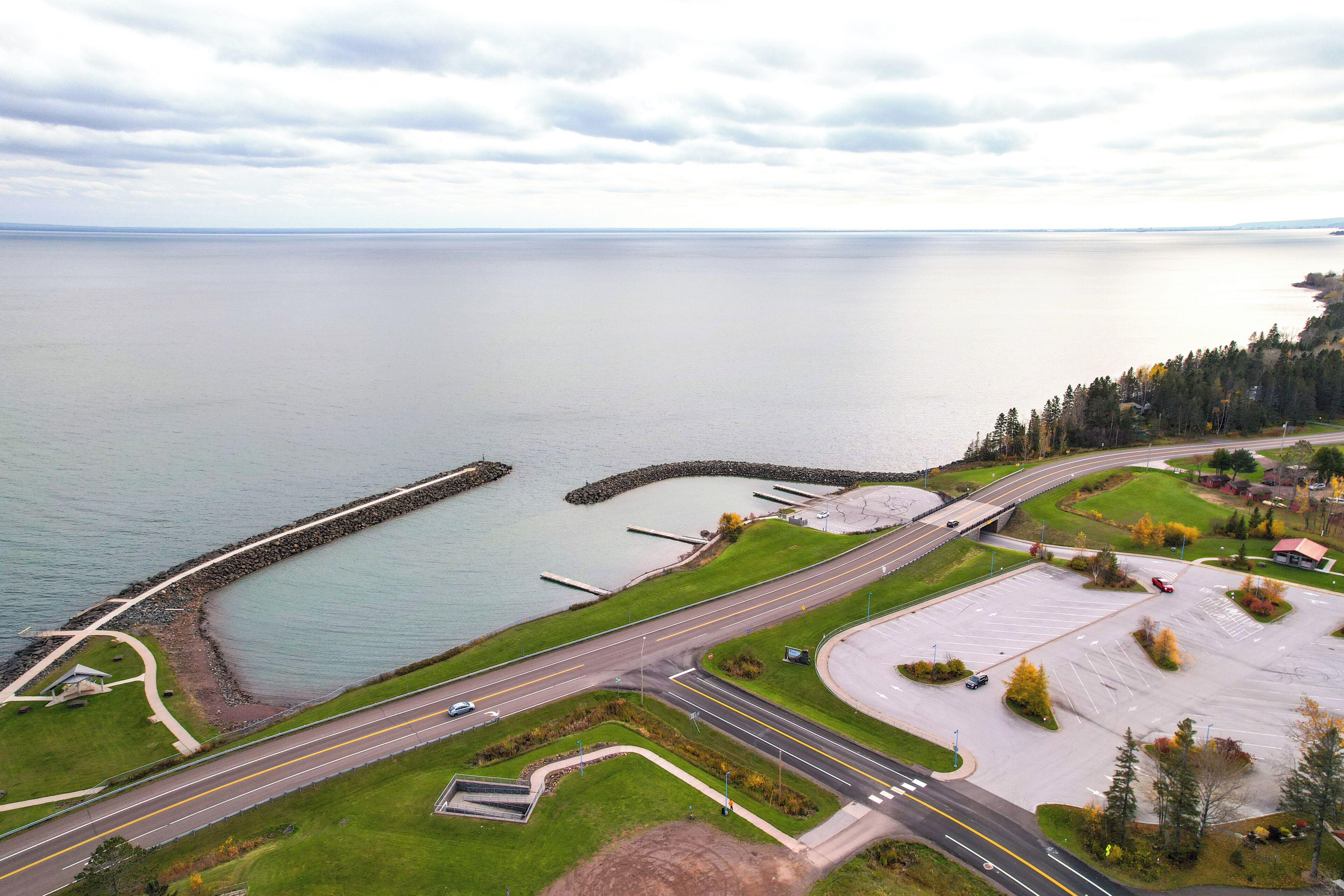 An aerial view of a coastal area with a parking lot, roads, and a body of water.