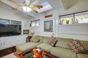 A living room with a sectional sofa, a ceiling fan, a flat-screen TV, and a window with decorative items. - Spacious Bryan Vacation Rental w/ Pool & Patio! (Bryan)