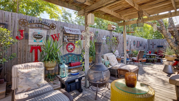 A covered outdoor patio with wooden furniture, a large decorative vase, and a welcome sign. - Spacious Bryan Vacation Rental w/ Pool & Patio! (Bryan)