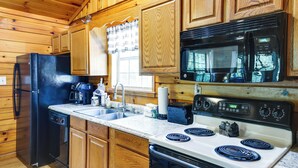 A kitchen with wooden cabinets, a black refrigerator, a microwave, a stove, and a sink. - Tennessee Cabin w/ Balcony, Hot Tub & Pool Access! (Sevierville)