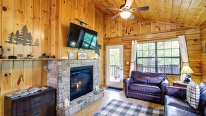 A cozy cabin interior with a stone fireplace, leather sofa, and a television mounted above it. - Tennessee Cabin w/ Balcony, Hot Tub & Pool Access! (Sevierville)