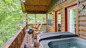 A wooden deck with a hot tub, outdoor furniture, and a view of the forest. - Tennessee Cabin w/ Balcony, Hot Tub & Pool Access! (Sevierville)